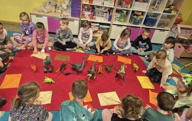 Dzieci siedzący dookoła wystawy dinozaur&oacute;w
