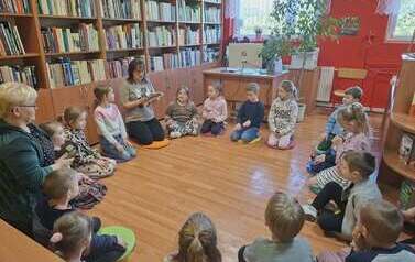 Dzieci siedzą w kole i słuchają pani bibliotekarki