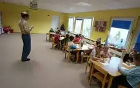 Dzieci siedzą przy stolikach i słuchają pani psycholog