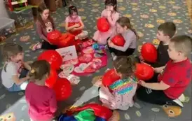 Dzieci siedzą w kole i trzymają balony w kształcie serc