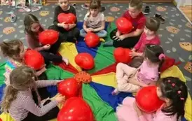 Dzieci siedzą na chuście animacyjnej trzymając balonowe serca