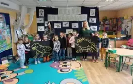 Dzieci z paniami prezentują wsp&oacute;lnie wykonanego dinozaura z makaronu