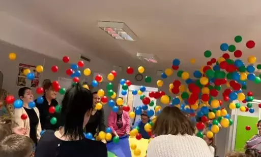 Rodzice z dziećmi podrzucają kolorowe piłeczki na chuście animacyjnej